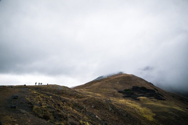 silhouette of people on mountain cliff facing fogs