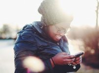 smiling woman wearing black coat using smartphone